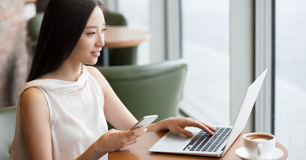 women using her phone and laptop at a cafe