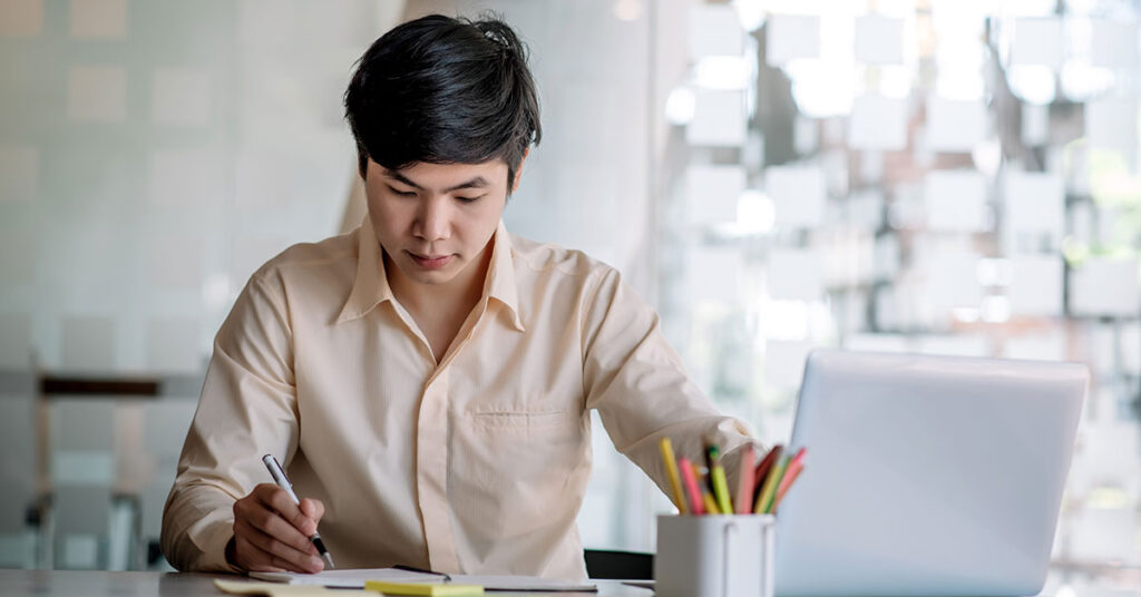 man working at his desk and writing his work on paper