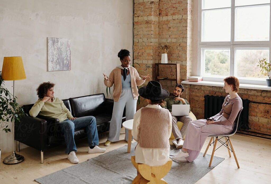 Smiling confident African-American team leader standing among colleagues and gesturing hands while explaining project plan at staff meeting in coworking space