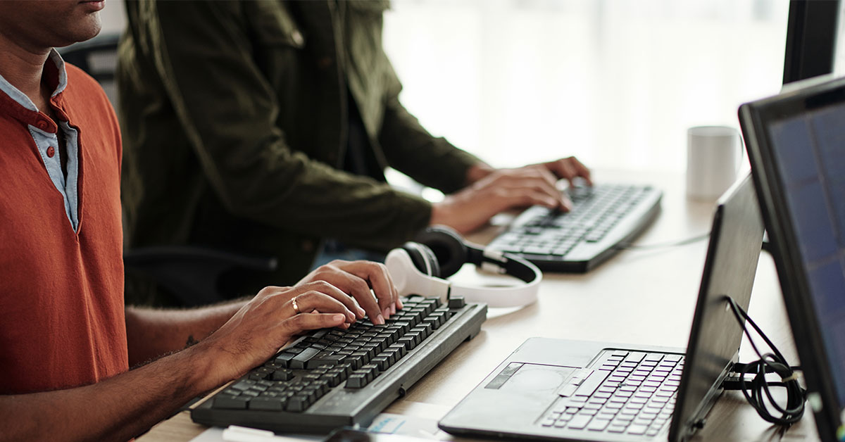 two people writing on their computers at work.