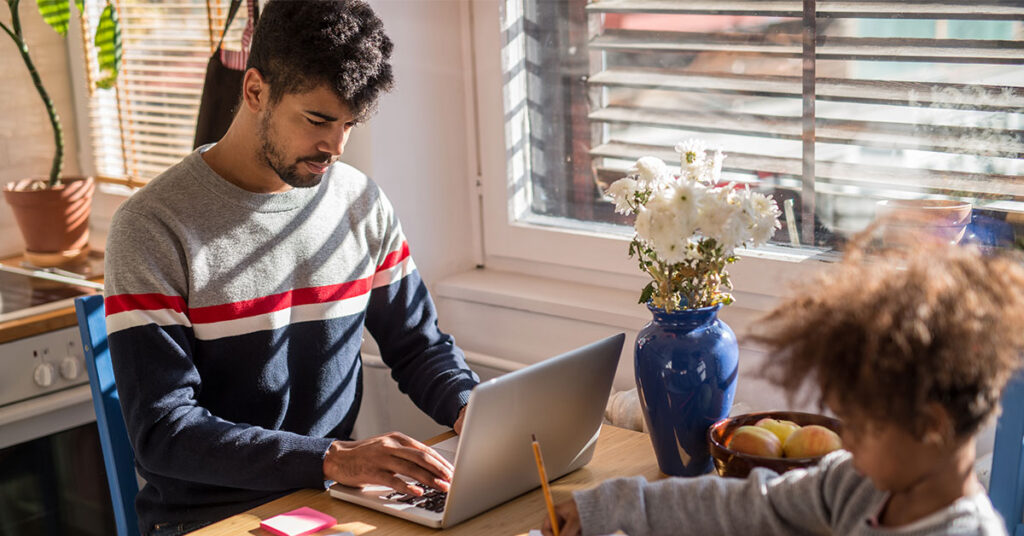 a man working from home with a child drawing at the same table