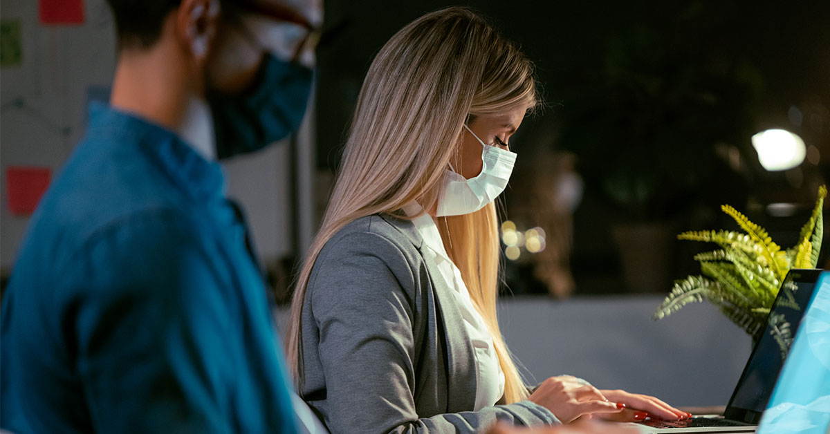 two people co-working in an office space with masks during the pandemic.