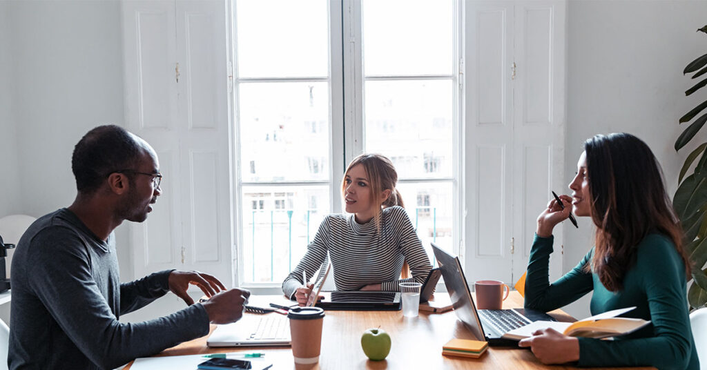 three co-workers discussing a project around a table at work