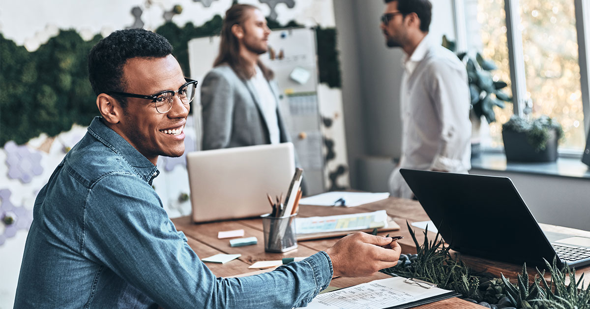 man sitting at desk while co-workers chat in background