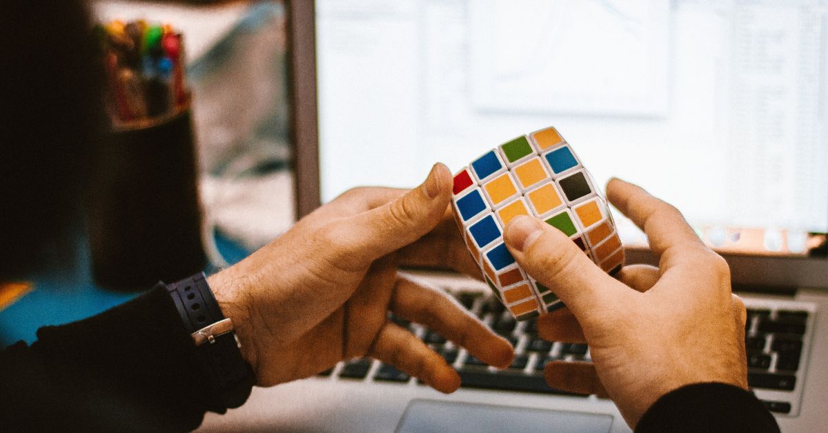 Two hands in front of a computer screen solve a complex Rubiks cube
