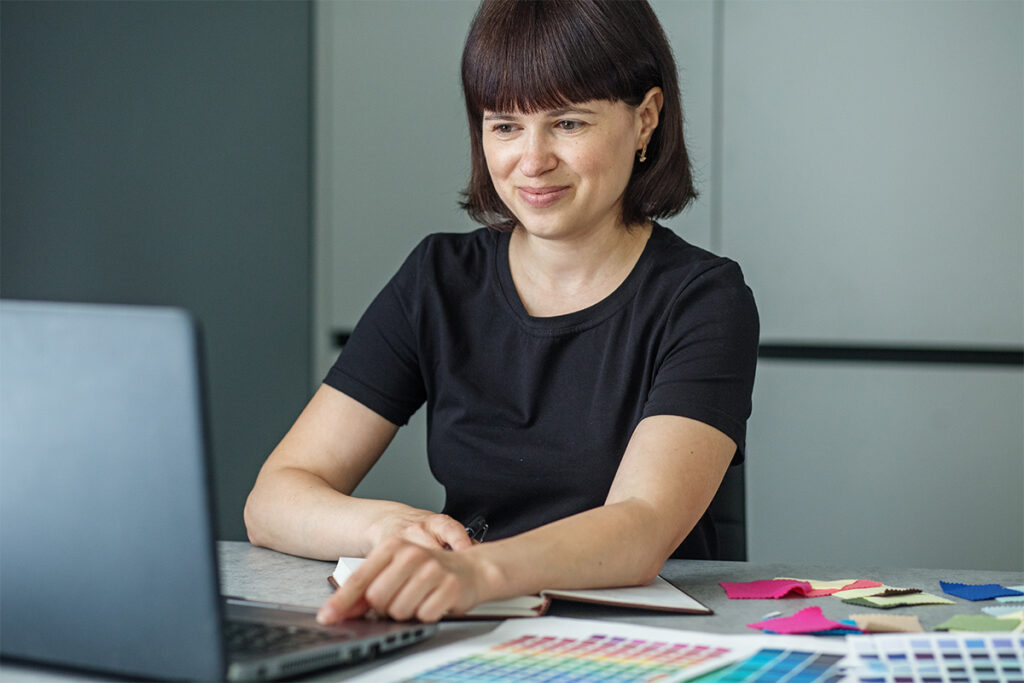 Successful woman plans work schedule, writes in notebook, sitting at workplace with laptop